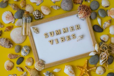 Kompozisyon kağıdı beyaz kağıt metin YAZI VİBES, deniz kabukları, çakıl taşları, sarı arka plan modeli. Boşluk, üst görünüm, durgun hayat, düzlük. Deniz seyahati konsepti turizm ve tatil beldeleri. Yaz tatili