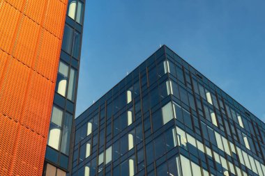 Gökyüzü arka planında cam cepheli modern ofis binası. Ofis binasının şeffaf cam duvarı, turuncu süslemeli. Modern Avrupa binasının dış cephesi