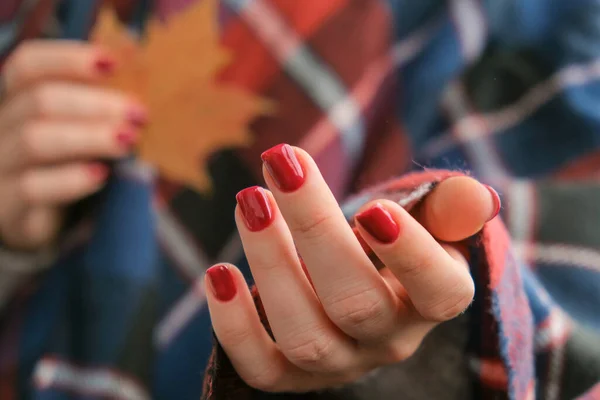 Stylish red female nails. Fall leaf in hands. Modern Beautiful manicure. Autumn winter nail design concept of beauty treatment. Gel nails. Skin care. Wellness. Trendy colors.