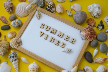 Kompozisyon kağıdı beyaz kağıt metin YAZI VİBES, deniz kabukları, çakıl taşları, sarı arka plan modeli. Boşluk, üst görünüm, durgun hayat, düzlük. Deniz seyahati konsepti turizm ve tatil beldeleri. Yaz tatili