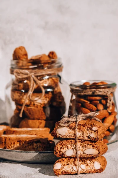 Traditional Italian cantuccini cookies with almonds in glass jar. Sweet dried biscuits. Homemade fresh Italian cookies cantuccini stacks and organic almond seeds. Healthy organic eating nutrition