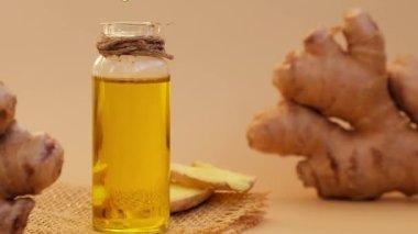 Cam şişe zencefil yağı, bej arka planda zencefil kökü. Sağlıklı yemek yeme konsepti. Zingiber officinale Temel Yağ. Dünya tonları cilt bakımı, vücut ve vücut için doğal kozmetik malzemeleri ve