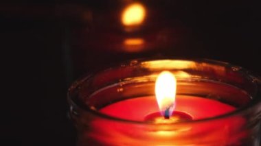 Kırmızı mum, cam bir şamdanda yanıyor. Kırmızı mum, alev alev yanan alevlerle yanıyor. Karanlık arka planda ateş dilleri. Sevgililer Günü, tutku, aşk, duygular, romantik ruh hali konsepti. Tek Renkli