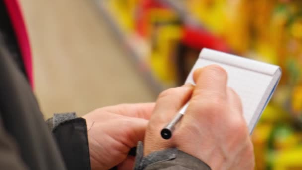 Female Hands Holding Paper Notebook Shopping List Blurred Shelves Background — Stock Video