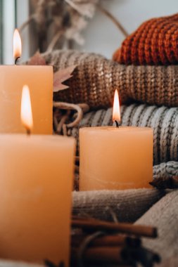 Hello Fall, celebrating autumn holidays at cozy home on the windowsill Hygge atmosphere Thanksgiving leaves, spices and candle on cozy knitted sweater in warm yellow lights. Selective focus Raining Outside the window