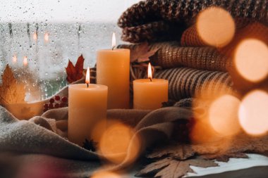 Merhaba güz, kış tatilini pencerenin kenarındaki evde kutluyoruz Şükran Günü atmosferinde Şükran Günü yaprakları, baharatlar ve sıcak sarı ışıkta örülmüş sıcak süveter üzerine mum. Pencerenin dışında Seçici Odaklanma Yağmuru