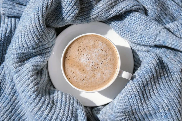 White cup of morning coffee on blue sweater background. Cozy home autumn concept. Aesthetics blog lifestyle. Still life concept. Cappuccino or latte hot drink. Top view flat lay
