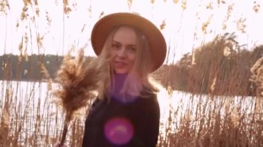 Kırsal kesimde bej şapkalı, siyah kazaklı, gülümseyen Avrupalı sarışın kadın. Altın saat, Cottagecore. Yerel seyahat. Yavaş yaşam. Akıl sağlığı. Toprak tonları. Pampas otu