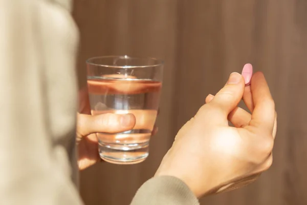 Female hand holding glass of water and pink pill. Collagen supplement for nutrition. Healthy eating lifestyle. Taking vitamins or nutritional supplements. Preventive medicine. Healthcare and wellbeing