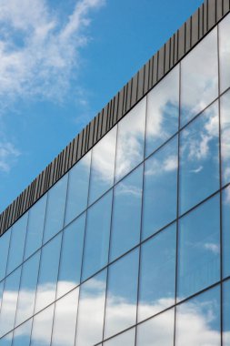 Gökyüzü arka planında cam cepheli modern ofis binası. Ofis binasının cam duvarında bulutların yansıması var. Modern Avrupa binasının dış cephesi