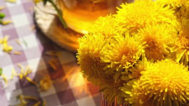 Karahindiba çiçeği cam çaydanlıkta sağlıklı çay ve masada cam bardak. Bahçe yakınlarındaki yaz gününde taze karahindiba çiçeklerinden dökülen lezzetli bitkisel çay. Yeşil açıklık Sıcak karahindiba çayı