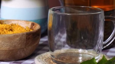 Karahindiba çiçeği cam çaydanlıkta sağlıklı çay ve masada cam bardak. Bahçe yakınlarındaki yaz gününde taze karahindiba çiçeklerinden dökülen lezzetli bitkisel çay. Yeşil açıklık Sıcak karahindiba çayı