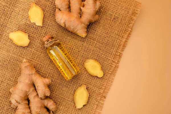Glass bottle of essential ginger oil, ginger root on beige background. Healthy food eating concept. Zingiber officinale Essential oil. Earth tones Natural cosmetics ingredients for skincare, body and hair care Top view
