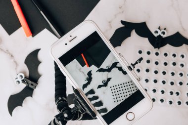 Cep telefonundan el yapımı kağıt yarasaların fotoğrafını çekiyor. Cadılar Bayramı süslemeleri. Mutlu Cadılar Bayramı partisi konsepti. Çocuk sanat projesi. Diy konsepti. Adım adım Zanaat