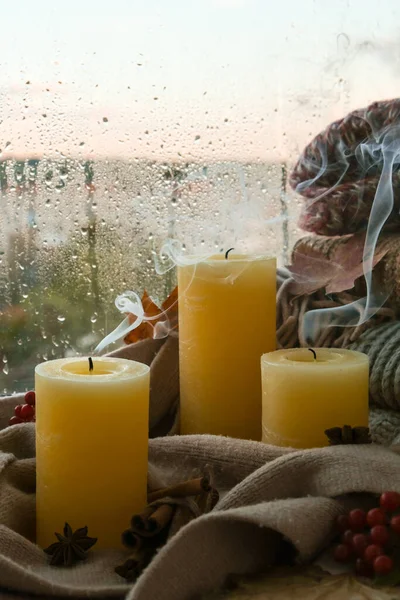 Blown candle with smoke Hello Fall, celebrating autumn holidays at cozy home on the windowsill Hygge atmosphere Thanksgiving leaves, spices and candle on cozy knitted sweater in warm yellow lights. Selective focus Raining Outside the window