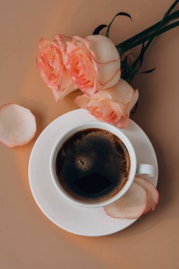 Vazoda pembe bir gül ve bej arka planda beyaz bir fincan kahve. Minimum bileşim. Romantik pastel pembe gül çiçeği. Modern estetik. Tarafsız toprak tonları. Tatil sabahı kahvaltısı yaratıcı