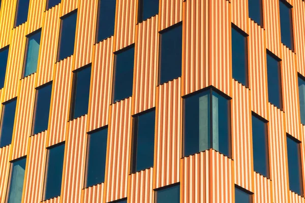 Modern office building exterior with glass facade on clear sky background. Transparent glass wall of office building with orange decoration. Element of facade of modern European building Commercial