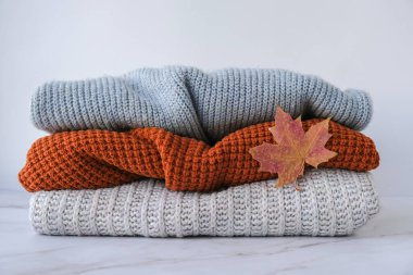 Sonbahar akçaağaç yaprağıyla örülmüş sıcak süveter yığını. Eski moda süveterler. Turuncu ve mavi renkler. Konforlu hygge konsepti Boşluğu kopyala Sonbahar sezonu