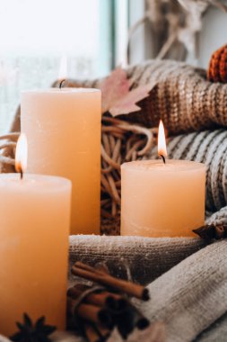 Hello Fall, celebrating autumn holidays at cozy home on the windowsill Hygge atmosphere Thanksgiving leaves, spices and candle on cozy knitted sweater in warm yellow lights. Selective focus Raining Outside the window