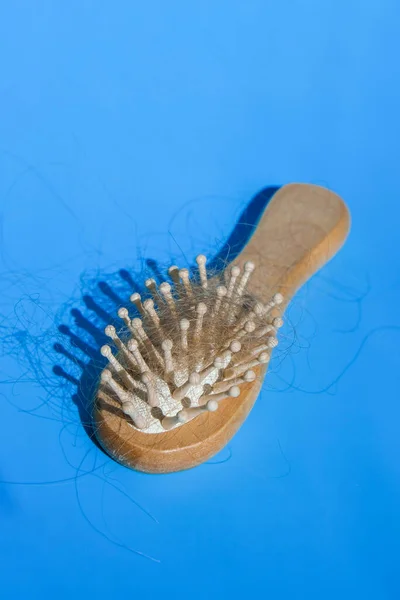Blonde hair loss problem with hairbrush on blue background. Alopecia, hair problem, falling hair on brush healthy medical treatment concept. Hormonal changes, unhealthy of aging