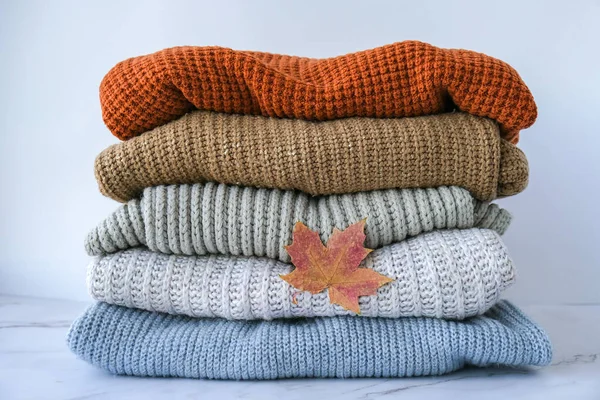 Stack of cozy knitted warm sweater with Autumn fall maple leaf. Sweaters in retro Style. Orange and blue colors. Cozy hygge concept Copy space Autumn season