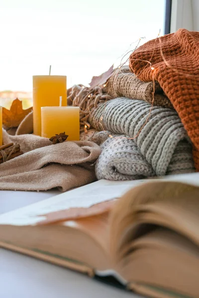 Book on first plan Thanksgiving and Hello Fall, celebrating autumn holidays at cozy home on the windowsill Hygge atmosphere Autumn leaves, spices and candle on cozy knitted sweater in warm yellow lights. Selective focus