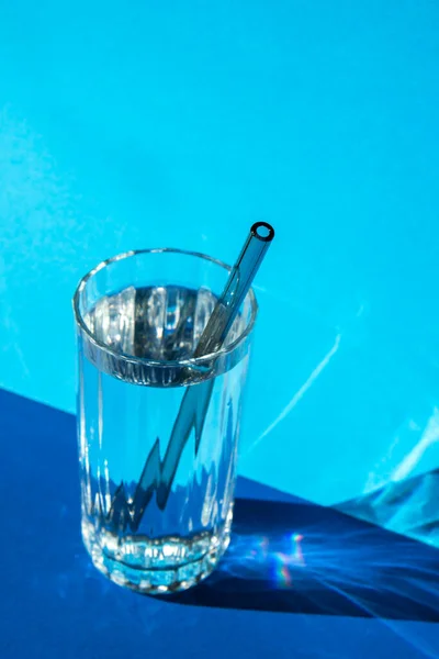 Reusable glass Straws in Glass with water on blue background Eco-Friendly Drinking Straw Set with cleaning brush. Zero waste, plastic free concept. Sustainable lifestyle. Waste free living Low waste