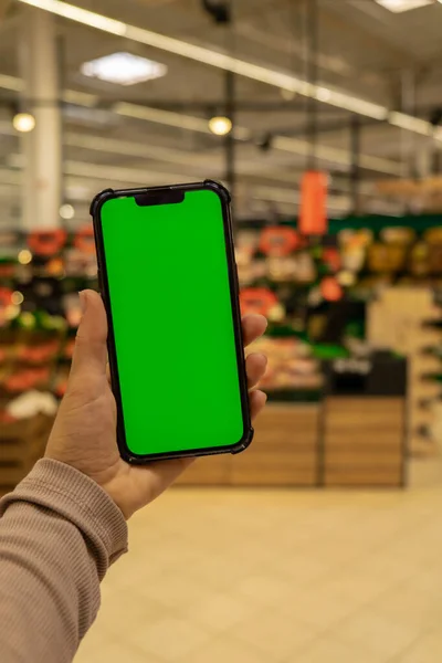 Mobile phone Chroma key. Close up of woman hand holds smart phone with green screen at shopping mall store. Buying food at supermarket, grocery shop center online. Department store. Gadgets