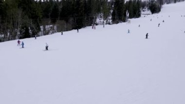 Skiers skiing downhill in winter resort mountains. Aerial top view of ski area. Skiers and snowboarders riding down the hill. Skiers and lifts in Carpathians alpine ski resort, majestic snowy winter