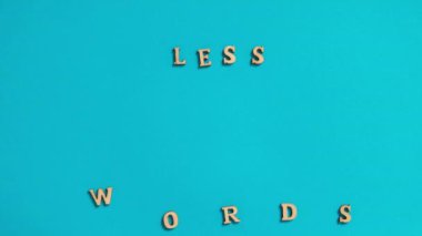 Time lapse of Quote LESS WORDS MORE ACTION made out of wooden letters on bright blue background. Motivational Words Quotes Concept. Text letters stop motion 4k footage 