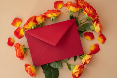 Beautiful red roses flowers in red postal envelope on neutral beige background, copy space for text, spring time, greeting card for holiday. Flower delivery. Delicate red yellow roses. Minimal trendy