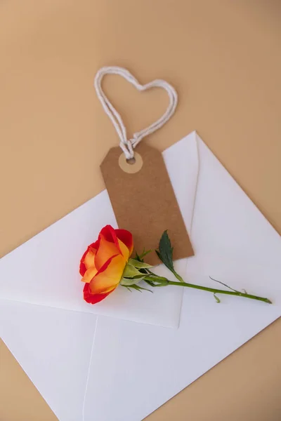Beautiful red roses flowers in postal envelope on neutral beige background, beige paper note with rope in heart shape copy space for text, spring time, greeting card for holiday. Flower delivery