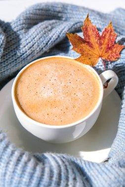 Akçaağaç sarısı yapraklı mavi örgü süveterin üzerinde beyaz bir sabah kahvesi. Konforlu ev konsepti. Estetik blog yaşam tarzı. Sonbahar sakin bir hayat. Cappuccino ya da latte sıcak içecek. Atmosfer