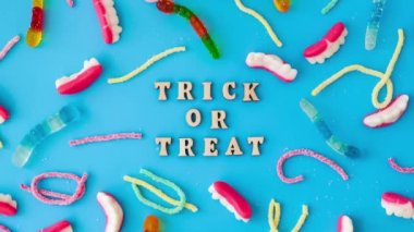 4k zoom in out Halloween concept. Halloween party decorations with words TRICK OR TREAT, sweets, top view flat lay on blue background. Greeting