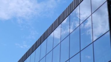 Gökyüzü arka planında cam cepheli modern ofis binası. Ofis binasının cam duvarında bulutların yansıması var. Modern Avrupa binasının dış cephesi