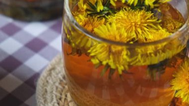 Karahindiba çiçeği cam çaydanlıkta sağlıklı çay ve masada cam bardak. Bahçe yakınlarındaki yaz gününde taze karahindiba çiçeklerinden dökülen lezzetli bitkisel çay. Yeşil açıklık Sıcak karahindiba çayı