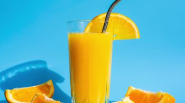 4k zoom in out Glass of fresh squeezing Orange juice with eco metal drinking straw sliced fruits on blue background. Fruit juice, fresh cold drink. Refreshment in summer. Clean eating, weight loss