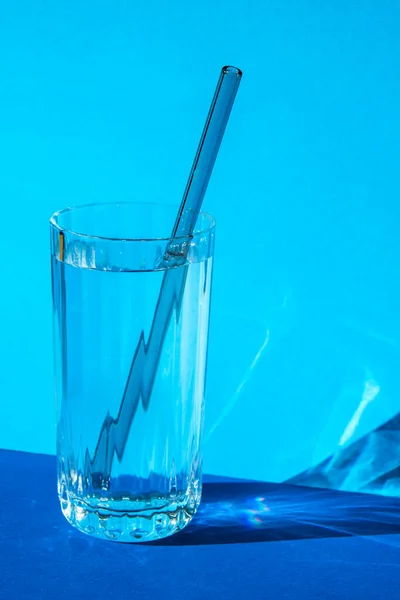 Reusable glass Straws in Glass with water on blue background Eco-Friendly Drinking Straw Set with cleaning brush. Zero waste, plastic free concept. Sustainable lifestyle. Waste free living Low waste