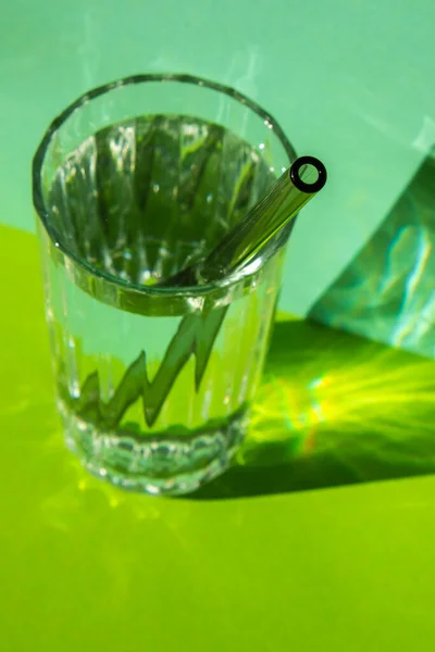 Reusable glass Straws in Glass with water on green background Eco-Friendly Drinking Straw Set with cleaning brush. Zero waste, plastic free concept. Sustainable lifestyle. Waste free living Low waste