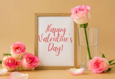 Mockup Wooden frame with text HAPPY VALENTINES DAY on delicate pink roses on beige background. Minimal trendy composition. Romantic pastel pink rose flowers. Neutral earth tones Greeting card holiday