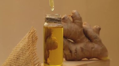 Esaslı zencefil yağı damlayan cam şişe, bej arka planda zencefil kökü. Sağlıklı alternatif yaşam. Zingiber officinale Earth tonları cilt bakımı, vücut ve saç için doğal kozmetik malzemeleri