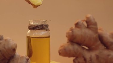 Esaslı zencefil yağı damlayan cam şişe, bej arka planda zencefil kökü. Sağlıklı alternatif yaşam. Zingiber officinale Earth tonları cilt bakımı, vücut ve saç için doğal kozmetik malzemeleri