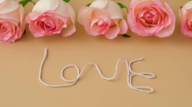 4k zoom in out Delicate pink rose on beige background. Word LOVE made of rope. Minimal trendy composition. Romantic pastel pink rose flower. Neutral earth tones. Greeting card for Valentines day