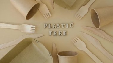 4k zoom in out PLASTIC FREE text around Eco friendly, disposable, recyclable, compostable tableware. Paper food boxes, dishes on neutral beige background. Sustainable lifestyle concept. Flat lay Earth
