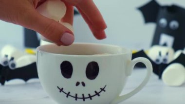 Female hand add marshmallow to painted scary jacks face white cup. Halloween diy concept Festive holiday decoration party Children handmade craft