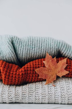 Sonbahar akçaağaç yaprağıyla örülmüş sıcak süveter yığını. Eski moda süveterler. Turuncu ve mavi renkler. Konforlu hygge konsepti Boşluğu kopyala Sonbahar sezonu