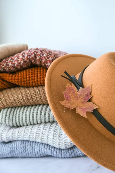 Stack of cozy knitted warm sweater with Autumn fall maple leaf and beige stylish hat. Sweaters in retro Style. Orange and blue colors. Cozy hygge concept Copy space Autumn season