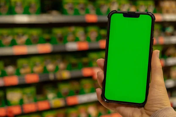 Mobile phone Chroma key. Close up of woman hand holds smart phone with green screen at shopping mall store. Buying food at supermarket, grocery shop center online. Department store. Gadgets