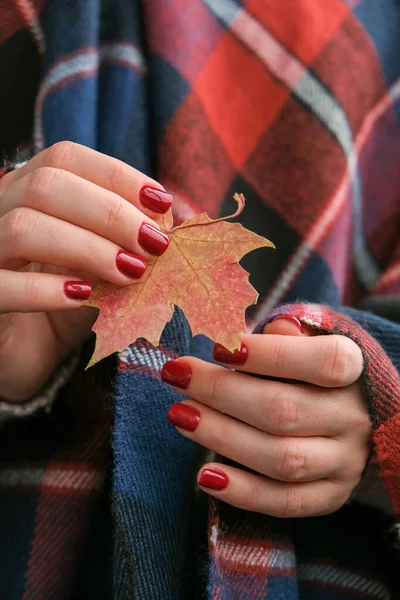 Stylish red female nails. Fall leaf in hands. Modern Beautiful manicure. Autumn winter nail design concept of beauty treatment. Gel nails. Skin care. Wellness. Trendy colors.