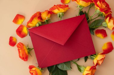 Beautiful red roses flowers in red postal envelope on neutral beige background, copy space for text, spring time, greeting card for holiday. Flower delivery. Delicate red yellow roses. Minimal trendy